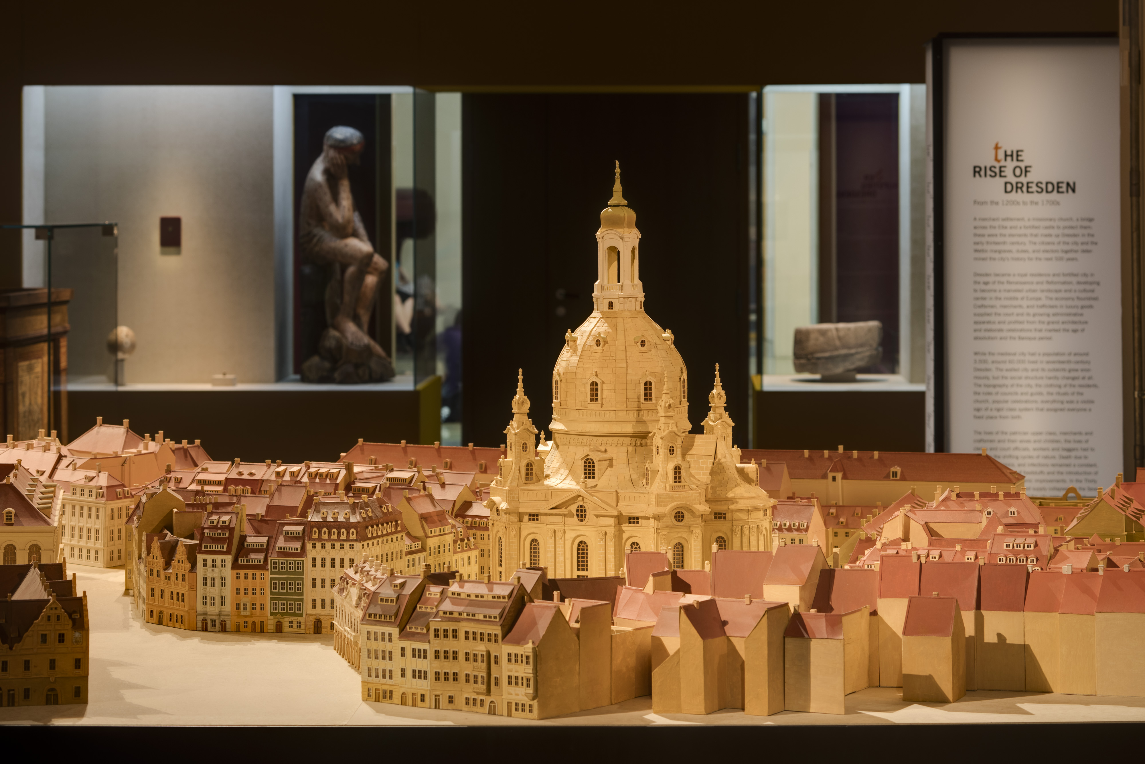 KI generiert: Das Bild zeigt ein detailliertes Modell einer historischen Stadt mit einer prominenten Kirche im Zentrum. Im Hintergrund befindet sich ein Ausstellungsraum, der der Geschichte Dresdens gewidmet ist.