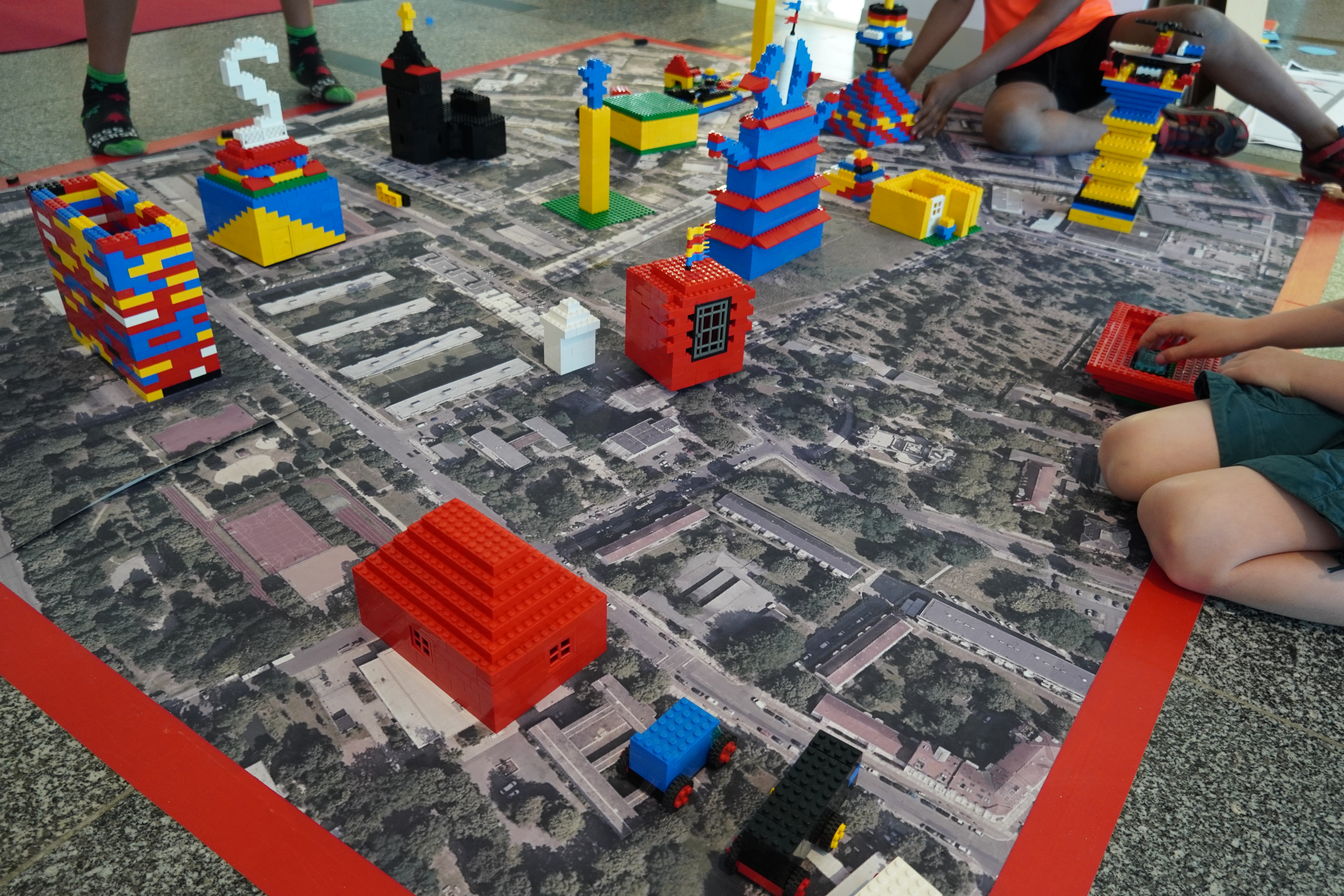 AI generated: The image shows children constructing various colourful buildings from Lego bricks on a map of a city or district. The main content is the creative design of an urban landscape with Lego bricks.