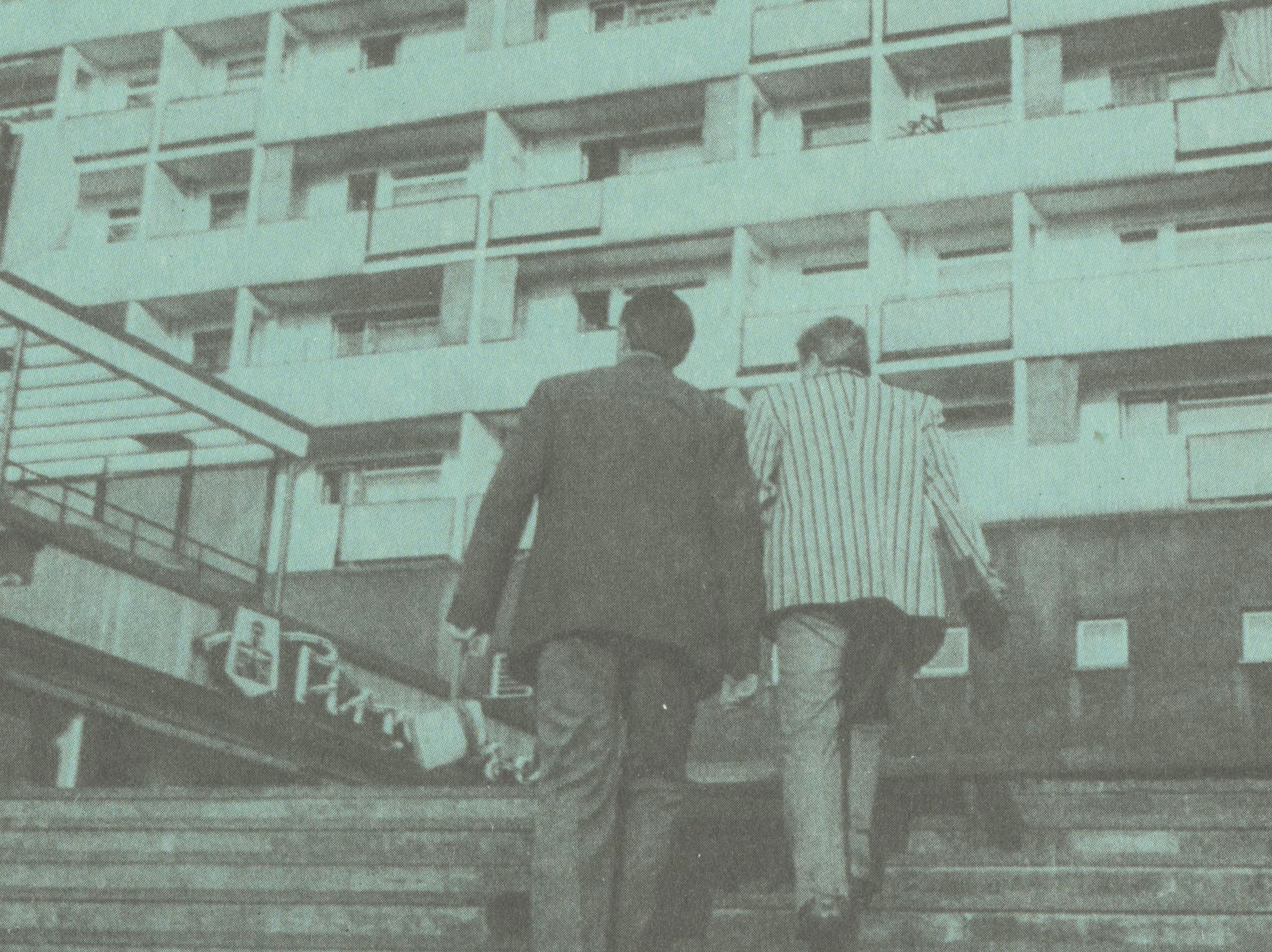 KI generiert: Das Bild zeigt ein hoch aufragendes sozialistisches Wohngebäude, vor dem zwei Personen eine Treppe hinaufgehen. Auf dem Gebäude steht ein Schriftzug und die Worte "Bau der sozialistischen Stadt" sowie "Rundgang 1" sind prominent zu sehen.