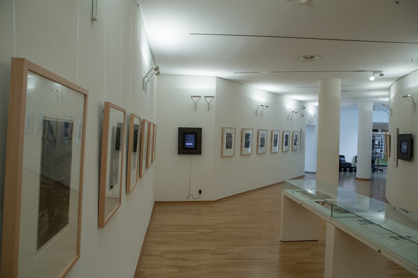 KI generiert: Das Bild zeigt eine Kunstgalerie mit gerahmten Fotografien an den Wänden und einem Glastisch in der Mitte des Raumes. Die Atmosphäre ist ruhig und gut beleuchtet, ohne Besucher.