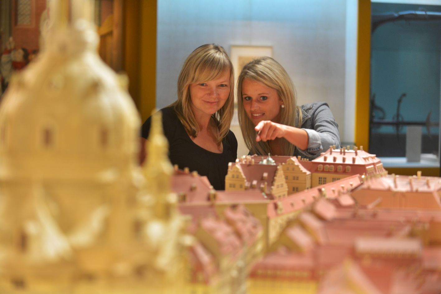 Zwei junge Frauen betrachten fasziniert ein historisches Stadtmodell von Dresden. Eine zeit auf die Frauenkirche.