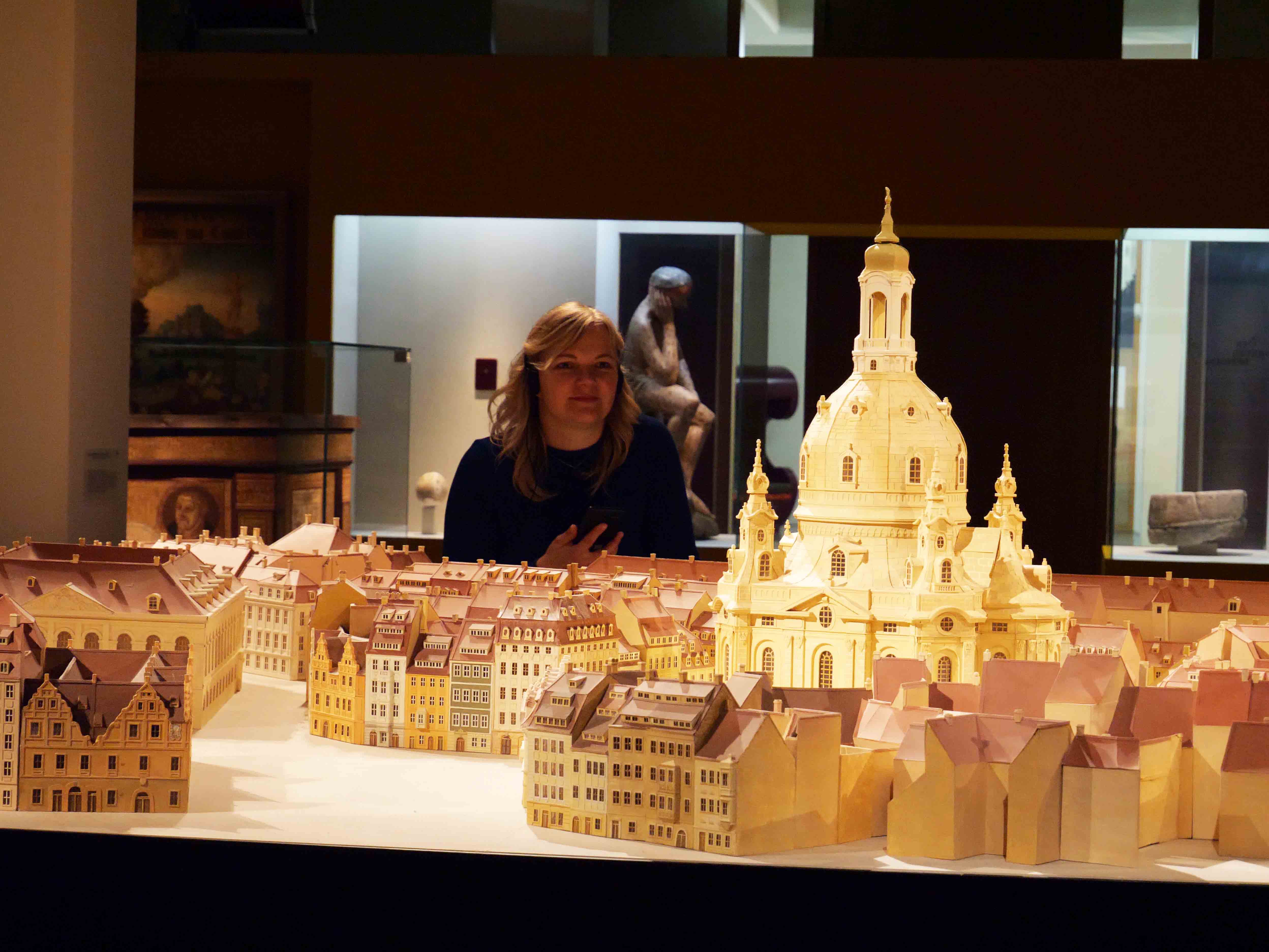 Museumsbesucherin betrachtet ein Satdtmodell mit Frauenkirche und hört sich dazu Informationen auf dem Audioguide an.
